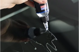 Hand trägt Reparaturharz aus Fläschchen auf einen Steinschlag in der Windschutzscheibe auf.