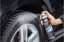 Hand sprüht Reifenglanz auf einen Autoreifen, Sprühnebel und Felge sind nah zu sehen.